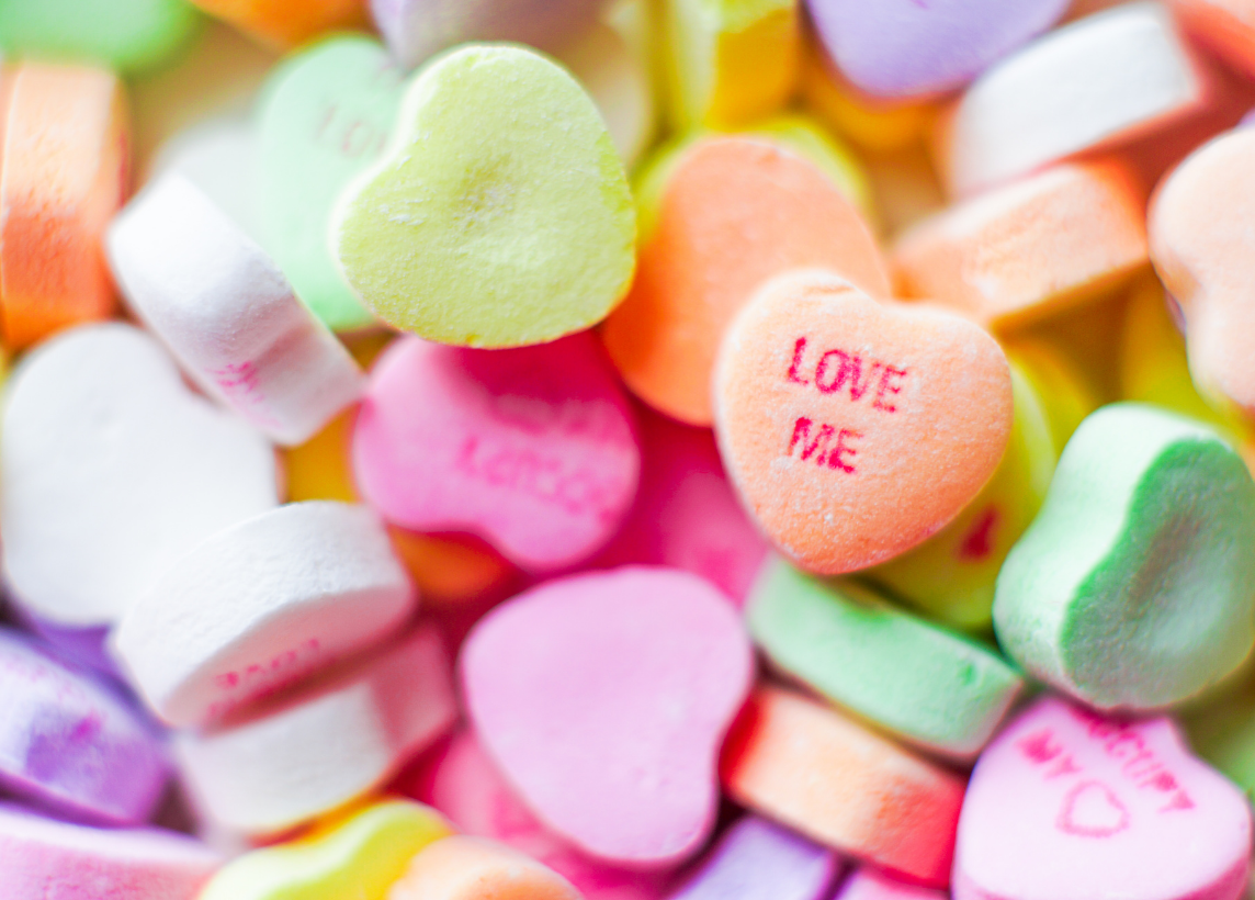 a pile of candy hearts with one legible one that reads "love me"