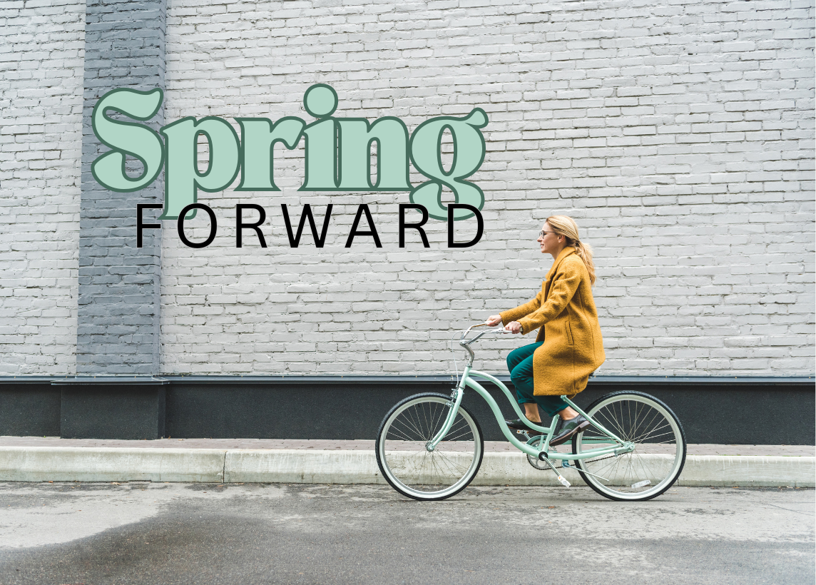 A woman riding a bike in front of a white brick building. The words "Spring Forward" sit in a large font on the upper right.