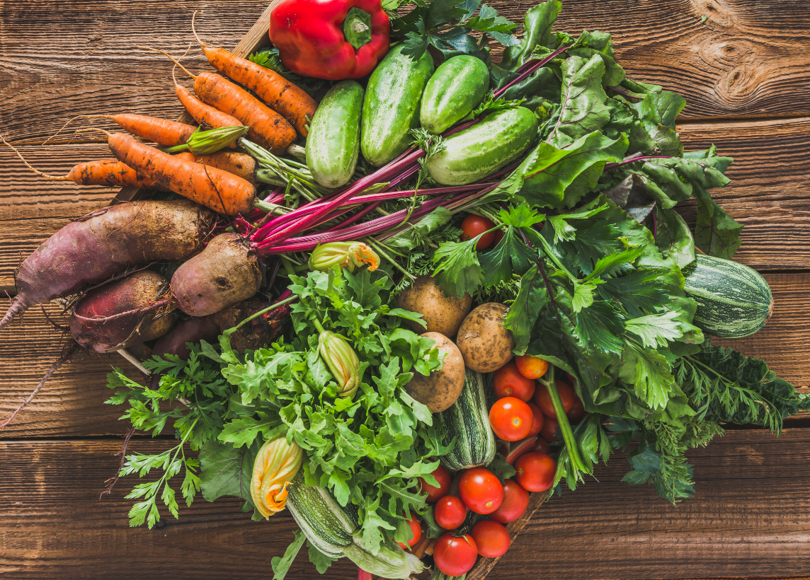 A variety of freshly picked vegetables on a wooden table including squash, carrots, potatoes, and tomatoes.