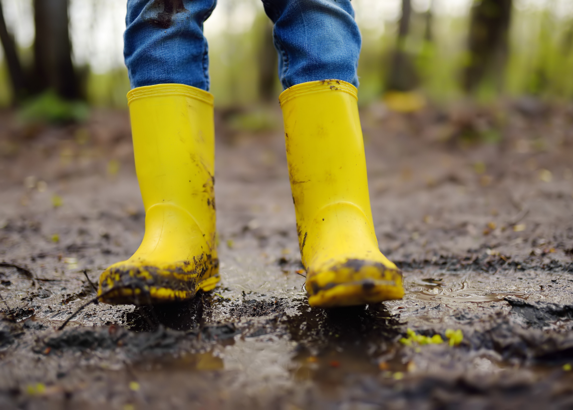 A close-up of a person wearing yellow rain boots while standing in the mud
