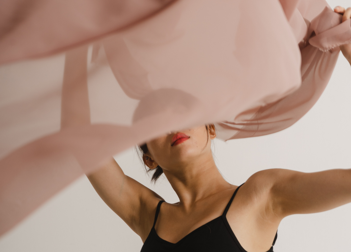 A dancer is captured mid-movement with a large, flowy, pink piece of fabric that slightly obscures her face.