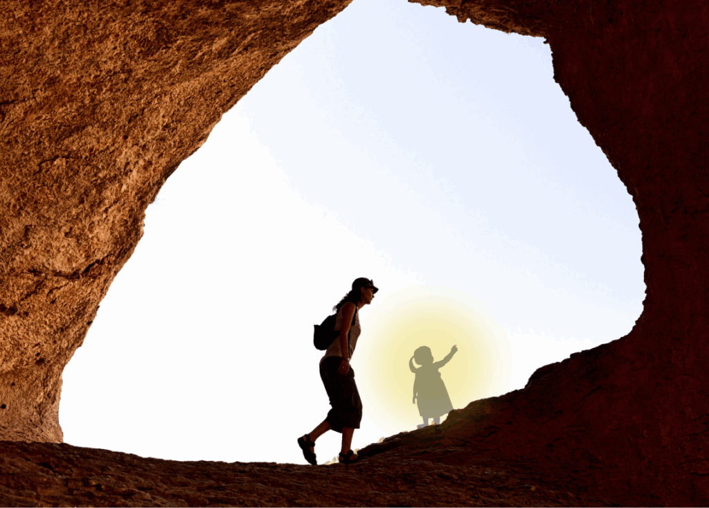 A glowing silhouette of a young girl points onward as a woman hikes along a naturally formed stone arch.